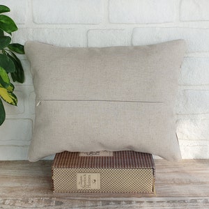 May include: A beige linen pillow with a zipper closure. The pillow is sitting on a book with a brown and white checkered pattern. The book has the text "The Complete Sherlock Holmes" on the spine.