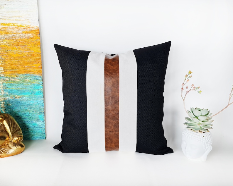 May include: Black and white striped cushion with a brown leather accent strip. The cushion is made of a soft, textured fabric.