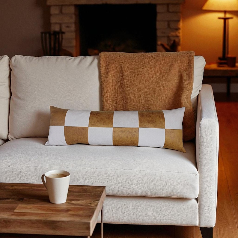 May include: A cream-colored sofa with a brown and white checkered lumbar pillow. A brown throw blanket is draped over the back of the sofa. A wooden coffee table with a white mug of coffee sits in front of the sofa.