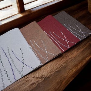 May include: Four placemats with embroidered floral designs. The placemats are in shades of brown, red, and gray.