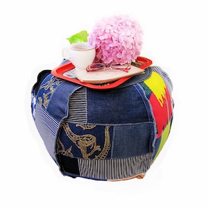 Könnte beinhalten: Ein runder, denimbezogener Hocker mit einem roten Tablett darauf. Auf dem Tablett befinden sich eine Tasse, Gläser und ein Buch. Eine rosa Blume liegt auf dem Buch. Der Hocker besteht aus verschiedenen zusammengenähten Denim-Stoffstücken.