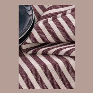 May include: A close-up of a burgundy and white striped fabric. The fabric is folded and has a subtle sheen.