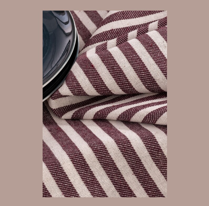 May include: A close-up of a burgundy and white striped fabric. The fabric is folded and has a subtle sheen.