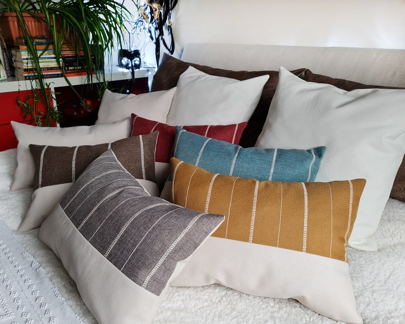 May include: A collection of decorative throw pillows with striped patterns in various colors, including brown, gray, teal, mustard yellow, and red. The pillows are arranged on a white bedspread.