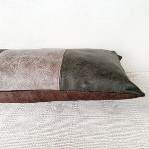 May include: A rectangular throw pillow featuring a color-blocked design with a light gray textured panel on the left, a dark olive green textured panel on the right, and a dark brown textured base panel running along the bottom edge.