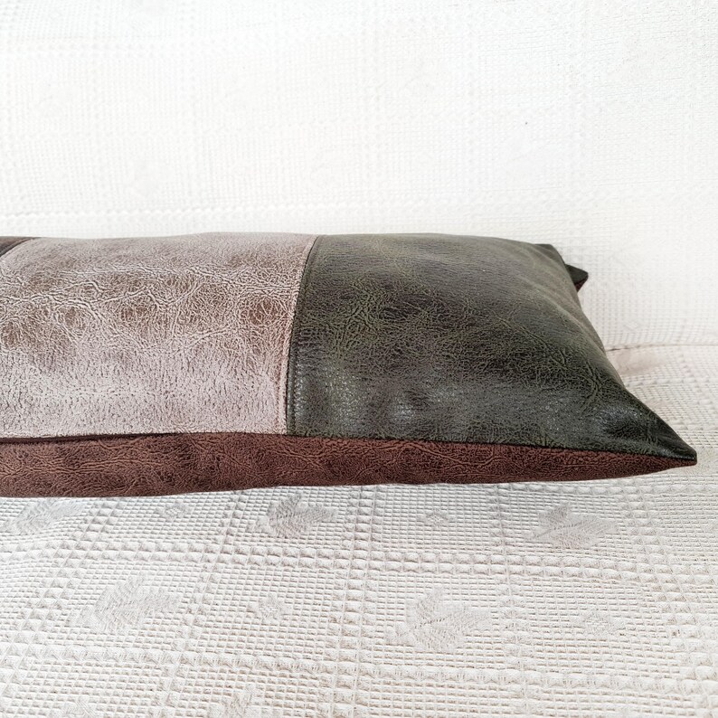 May include: A rectangular throw pillow featuring a color-blocked design with a light gray textured panel on the left, a dark olive green textured panel on the right, and a dark brown textured base panel running along the bottom edge.
