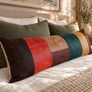May include: A long rectangular lumbar cushion featuring a patchwork design of faux leather panels in dark brown, bright red, tan, dark teal, and mustard yellow. The cushion has a visible textured surface and is stitched together in vertical and horizontal segments.