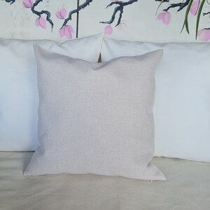 Puede incluir: Una almohada beige con una superficie texturizada sutil. La almohada est&aacute; colocada sobre una almohada blanca, que est&aacute; sobre un sof&aacute; beige.