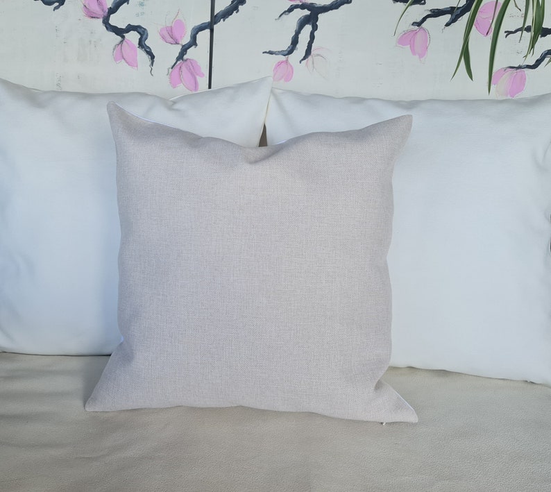 Puede incluir: Una almohada beige con una superficie texturizada sutil. La almohada est&aacute; colocada sobre una almohada blanca, que est&aacute; sobre un sof&aacute; beige.