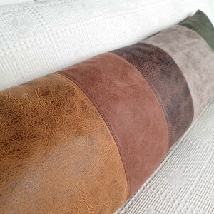 May include: A long, cylindrical bolster pillow featuring a color-blocked design with vertical panels in shades of textured tan, medium brown, dark brown, light gray, and olive green, all finished with a smooth, faux-leather appearance.