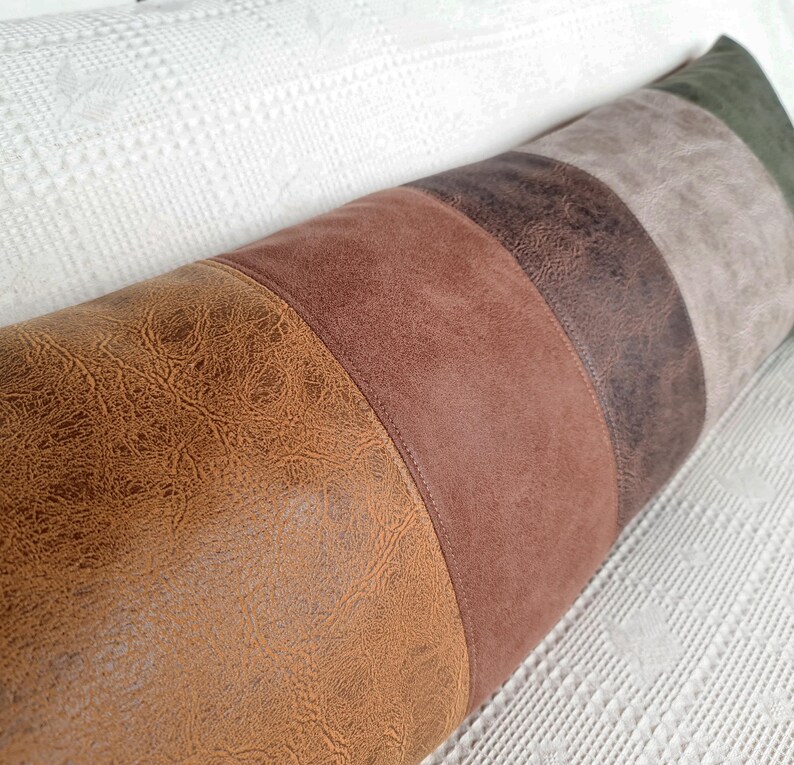 May include: A long, cylindrical bolster pillow featuring a color-blocked design with vertical panels in shades of textured tan, medium brown, dark brown, light gray, and olive green, all finished with a smooth, faux-leather appearance.