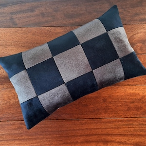 Puede incluir: Un coj&iacute;n rectangular decorativo con un dise&ntilde;o de tablero de ajedrez. El coj&iacute;n presenta cuadrados alternos de tela azul marino y gris. El coj&iacute;n est&aacute; colocado sobre una superficie de madera.