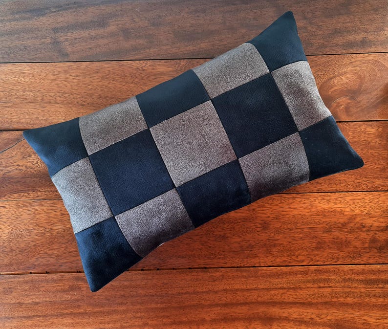 Puede incluir: Un coj&iacute;n rectangular decorativo con un dise&ntilde;o de tablero de ajedrez. El coj&iacute;n presenta cuadrados alternos de tela azul marino y gris. El coj&iacute;n est&aacute; colocado sobre una superficie de madera.