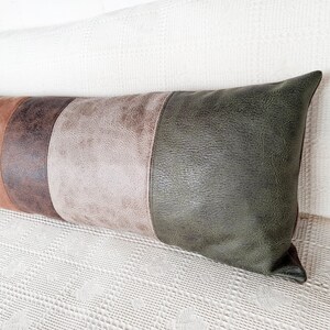 May include: A long rectangular lumbar pillow featuring a color-blocked design with vertical panels of textured faux leather in shades of dark brown, light tan, and deep olive green, finished with visible stitching along the seams.