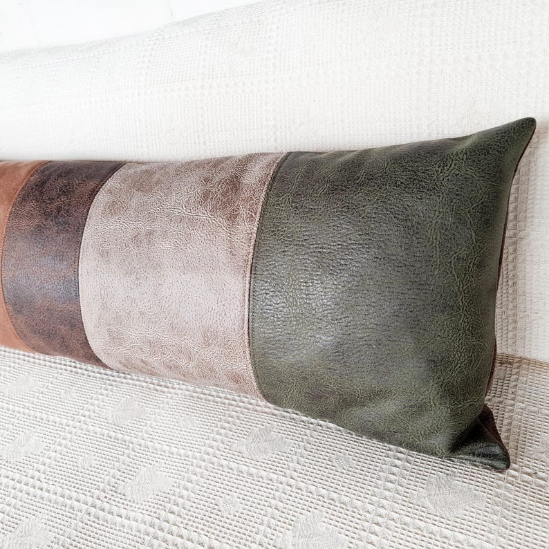 May include: A long rectangular lumbar pillow featuring a color-blocked design with vertical panels of textured faux leather in shades of dark brown, light tan, and deep olive green, finished with visible stitching along the seams.