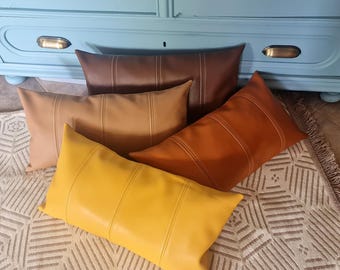 May include: A collection of rectangular throw pillows in various shades of brown and yellow. Each pillow has vertical stitched lines and a smooth, leather-like texture. The pillows are arranged on a patterned rug.