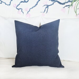 Puede incluir: Una almohada azul oscuro con tejido texturizado. La almohada est&aacute; sobre un sof&aacute; blanco.
