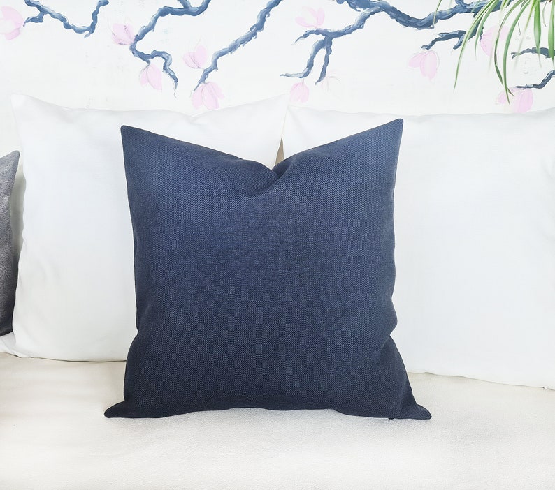 Puede incluir: Una almohada azul oscuro con tejido texturizado. La almohada est&aacute; sobre un sof&aacute; blanco.