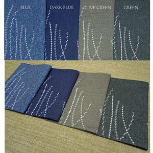 May include: Four placemats in blue, dark blue, olive green, and green with a white embroidered floral design. The placemats are laid out on a beige surface.