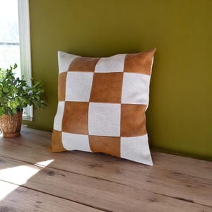 May include: A brown and white checkered throw pillow with a square pattern. The pillow is made of a soft, textured fabric.