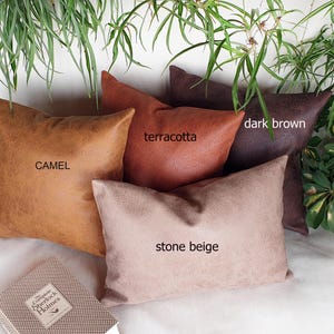 May include: Four decorative throw pillows in different colors and textures. The pillows are camel, terracotta, dark brown, and stone beige. The pillows are arranged on a white surface.