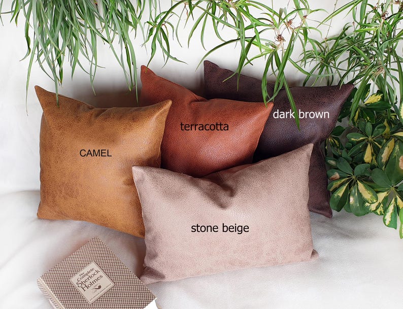 May include: Four decorative throw pillows in different colors and textures. The pillows are camel, terracotta, dark brown, and stone beige. The pillows are arranged on a white surface.