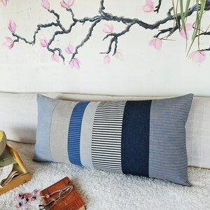 May include: A long rectangular pillow with a striped pattern in shades of gray, blue, and white. The pillow is made of a soft, textured fabric and has a subtle sheen.