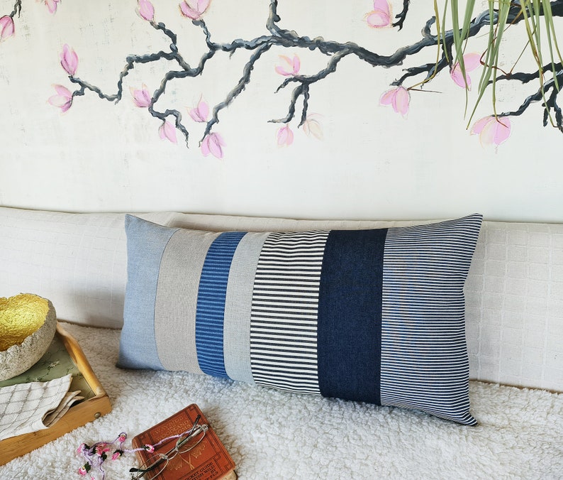 May include: A long rectangular pillow with a striped pattern in shades of gray, blue, and white. The pillow is made of a soft, textured fabric and has a subtle sheen.