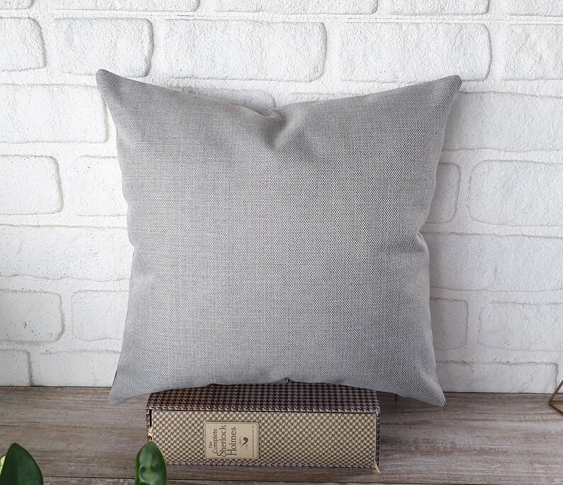May include: A gray square pillow with a textured fabric surface. The pillow is sitting on a brown and white checkered box.