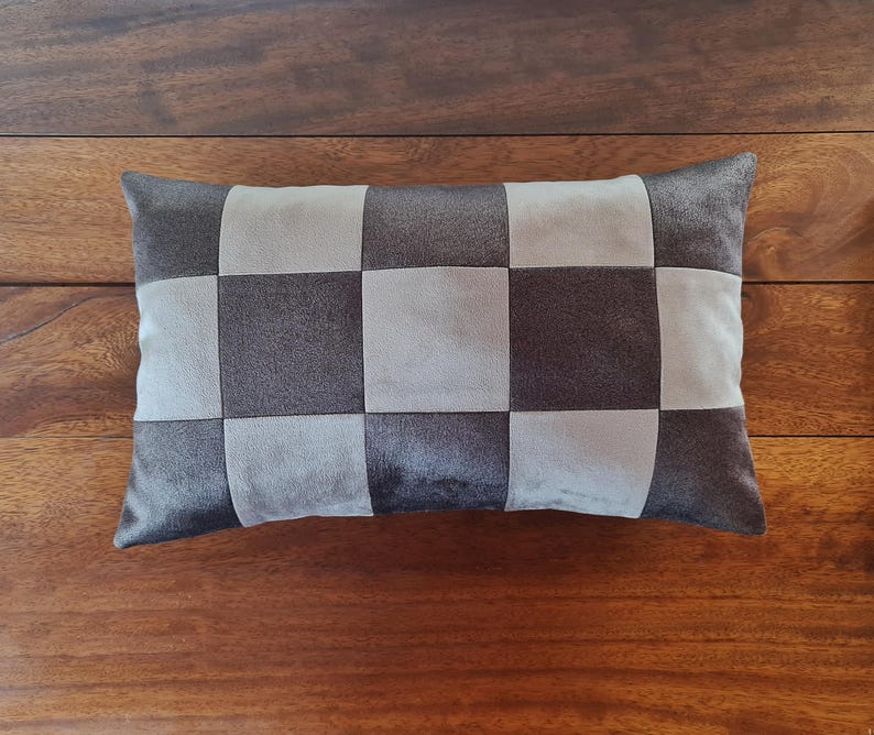 May include: A rectangular decorative pillow with a checkerboard pattern. The pillow features alternating squares of dark gray and light gray fabric. The pillow is placed on a wooden surface.