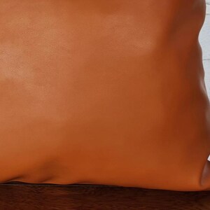 May include: A brown leather pillow with a smooth surface. The pillow is square and has a subtle sheen.