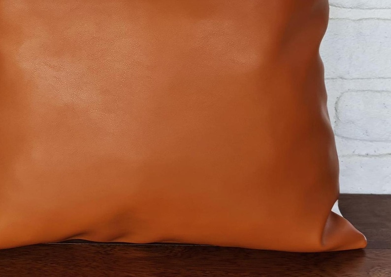 May include: A brown leather pillow with a smooth surface. The pillow is square and has a subtle sheen.