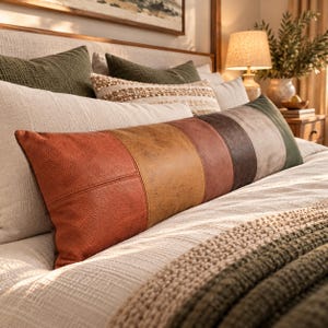 May include: A long rectangular lumbar pillow featuring a color-blocked design with vertical panels in shades of burnt orange, mustard yellow, terracotta, dark brown, and olive green, crafted from a textured material resembling leather.