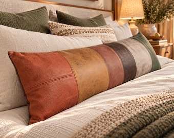 May include: A long rectangular lumbar pillow featuring a color-blocked design with vertical panels in shades of burnt orange, mustard yellow, terracotta, dark brown, and olive green, crafted from a textured material resembling leather.