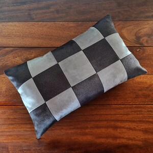 May include: A rectangular decorative pillow with a checkerboard pattern. The pillow features alternating squares of dark gray and light gray fabric. The pillow is placed on a wooden surface.