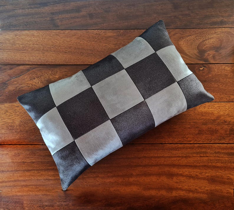 May include: A rectangular decorative pillow with a checkerboard pattern. The pillow features alternating squares of dark gray and light gray fabric. The pillow is placed on a wooden surface.