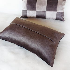 Puede incluir: Dos cojines decorativos. El coj&iacute;n delantero es rectangular, de tejido marr&oacute;n oscuro texturizado con una costura central. El segundo coj&iacute;n presenta un estampado a cuadros en tonos marrones y grises.