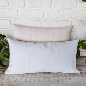 May include: Two decorative throw pillows with a textured fabric. The top pillow is a light beige color and the bottom pillow is white.