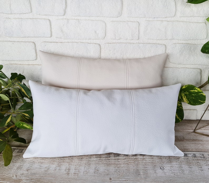 May include: Two decorative throw pillows with a textured fabric. The top pillow is a light beige color and the bottom pillow is white.