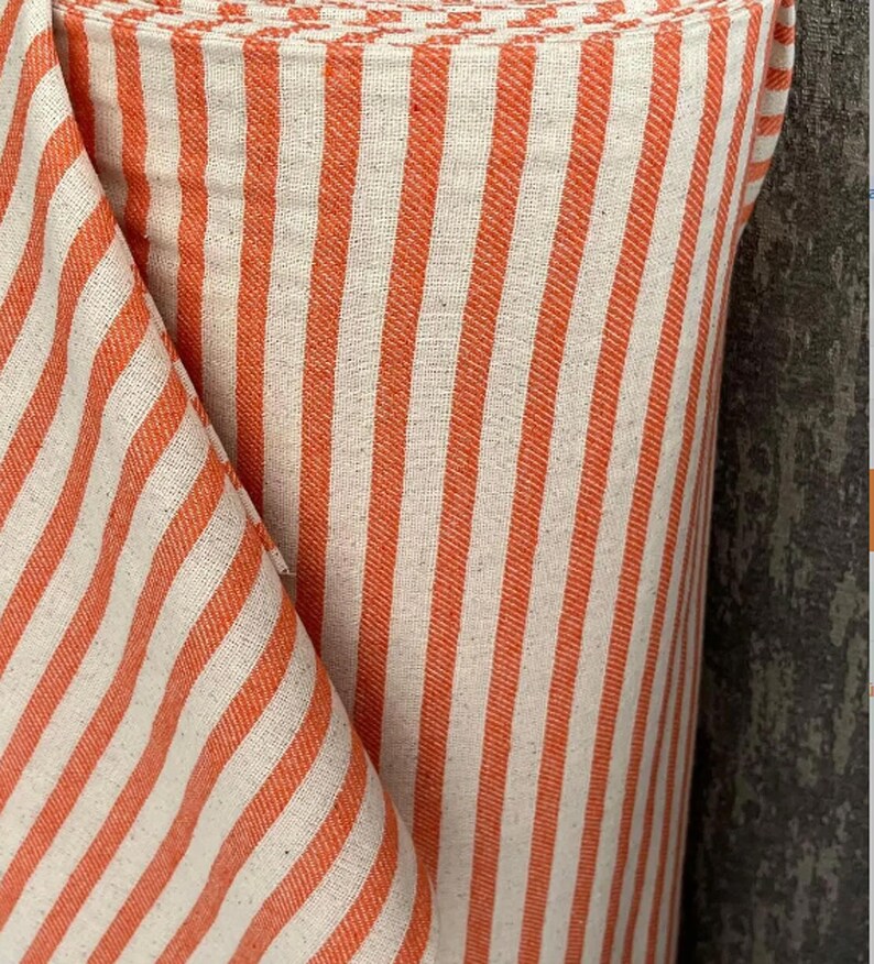 May include: Orange and white striped fabric with a subtle texture. The fabric is rolled up and the stripes are vertical.
