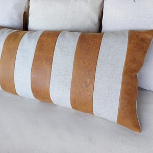 May include: A long, rectangular throw pillow with brown and white stripes. The pillow is made of a soft, textured fabric and has a subtle sheen.