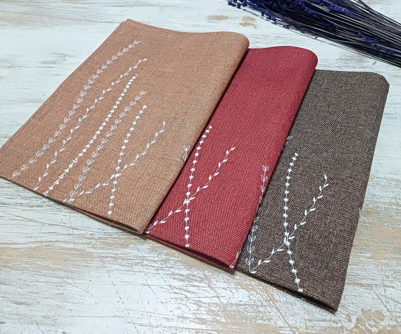 May include: Three placemats with a white embroidered design of branches and leaves on a brown, red, and beige background.