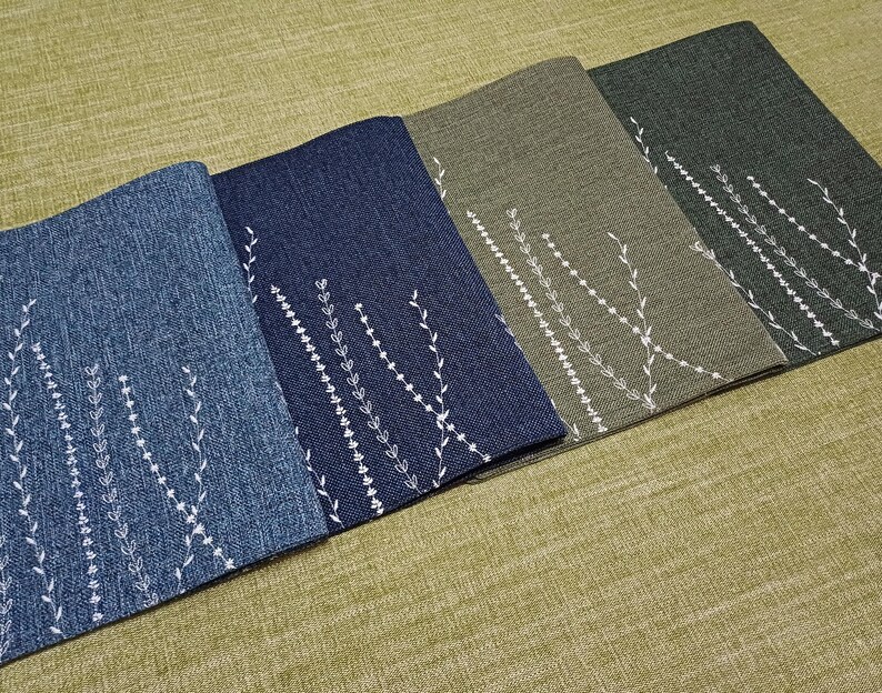 May include: Four placemats with a white floral design on a textured fabric background. The placemats are in shades of blue, green, and brown.