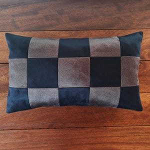 Puede incluir: Coj&iacute;n decorativo rectangular con un patr&oacute;n de tablero de ajedrez. El coj&iacute;n presenta cuadrados alternos de tela azul marino oscuro y gris. El coj&iacute;n est&aacute; colocado sobre una superficie de madera.