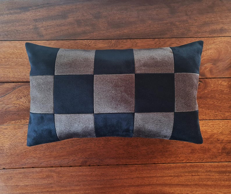 Puede incluir: Coj&iacute;n decorativo rectangular con un patr&oacute;n de tablero de ajedrez. El coj&iacute;n presenta cuadrados alternos de tela azul marino oscuro y gris. El coj&iacute;n est&aacute; colocado sobre una superficie de madera.