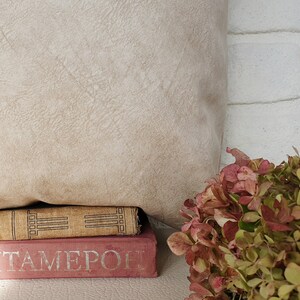 May include: A stack of two books with a beige pillow behind them. The top book has a brown cover with a gold design and the bottom book has a pink cover with the word "ITAMERO" printed in silver. A bouquet of pink and green flowers is in the foreground.
