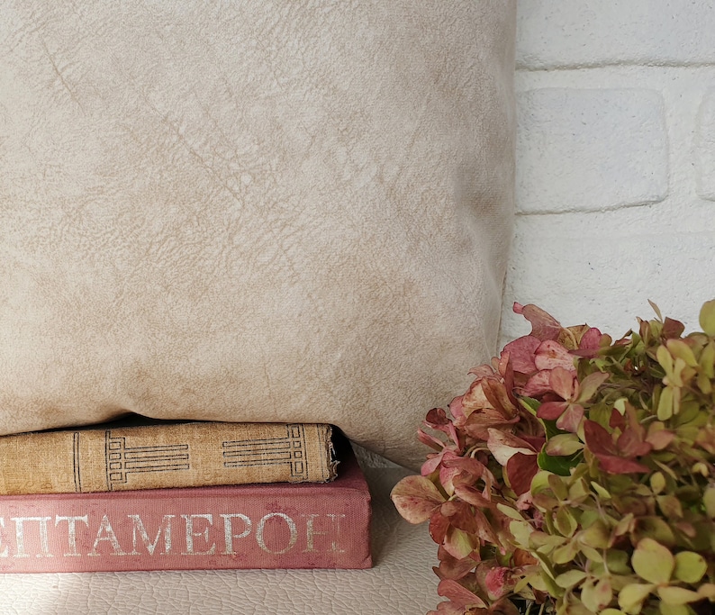 May include: A stack of two books with a beige pillow behind them. The top book has a brown cover with a gold design and the bottom book has a pink cover with the word "ITAMERO" printed in silver. A bouquet of pink and green flowers is in the foreground.