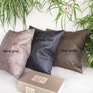 May include: Three decorative throw pillows in stone gray, smoky blue, and olive green. The pillows are made of a soft, textured fabric and are arranged on a white surface.