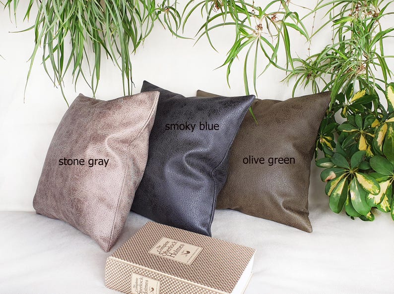 May include: Three decorative throw pillows in stone gray, smoky blue, and olive green. The pillows are made of a soft, textured fabric and are arranged on a white surface.