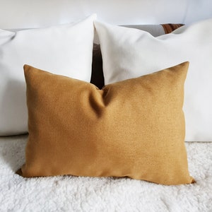 May include: Three throw pillows, one mustard yellow and two white, arranged on a white fluffy surface.
